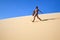 Beautiful girl in the desert goes on a hill barefoot on the sand with a hat and shoes in her hands