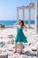 A beautiful girl in a dress, hat and sunglasses poses with a view of the ruins of the ancient Roman temple of Apolon. Side, Turkey