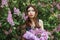 Beautiful girl in a dress posing near a Bush of lilacs on a summer day, purple flowers in the Park. Spring portrait of a girl