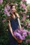 Beautiful girl in a dress posing near a Bush of lilacs on a summer day, purple flowers in the Park. Spring portrait of a girl