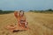 A beautiful girl in a dress sits on a wheat field. Fabulous photo of a blonde outside the city. A woman without allergies holds