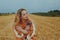 A beautiful girl in a dress sits on a wheat field. Fairytale portrait of a blonde outside the city. Girl without allergies holding