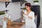 Beautiful girl dressed in white bathrobe pours milk from a carafe into a glass, in the stylish cozy kitchen. Healthy