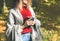 Beautiful girl drinking coffee in autumn wood. A cup with hot drink. Cosy mood. Red and yellow leaves. Beautiful nature. Stylish