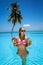 Beautiful girl in elegant bikini is standing in the pool and holding colorful fruity drink. Sexy woman in sequin bikini is posing