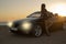 Beautiful girl in elegant dress posing beside a cabriolet on sunset