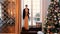 A beautiful girl in an evening dress and a black mink coat comes into the room decorated with a Christmas tree.