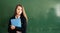 Beautiful girl with folder in hand on school green chalkboard background. Online education and e-learning concept. Back to school