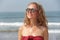 Beautiful girl freak in a red dress and blond hair, on the background of the sea. Summer girl in round wooden glasses. Unusual