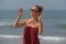 Beautiful girl freak in a red dress and blond hair, on the background of the sea. Summer girl in round wooden glasses. Unusual