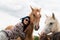 A beautiful girl in glasses and with a bandana on her head strokes the horses in the meadow. Blurred background