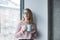 beautiful girl in the glasses stands in the wall near the window with a cup of coffee