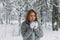 A beautiful girl in a gray jacket and knitted white mittens is drinking a drink in a snowy forest. Comfort and warmth in the