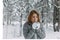 A beautiful girl in a gray jacket and knitted white mittens is drinking a drink in a snowy forest. Comfort and warmth in the