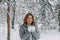 A beautiful girl in a gray jacket and knitted white mittens is drinking a drink in a snowy forest. Comfort and warmth in the