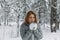 A beautiful girl in a gray jacket and knitted white mittens is drinking a drink in a snowy forest. Comfort and warmth in the