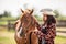 Beautiful girl in a hat and checkered shirt talks to calm a paint horse out in a ranch