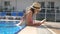 Beautiful girl in hat and sunglasses reading book at pool. Young woman relaxing at warm sunny day during vacation