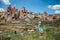 a beautiful girl in a hat and a turquoise dress stands in a meadow against the backdrop of the relief of capadocia