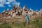 a beautiful girl in a hat and a turquoise dress stands in a meadow against the backdrop of the relief of capadocia