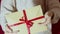 Beautiful girl holds out a gift envelope with a red ribbon. Beautiful girl hands hold a gift envelope with a red ribbon