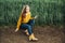 Beautiful girl with jeans, a yellow sweater and boots sits near an early wheat field