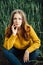 Beautiful girl with jeans, a yellow sweater and boots sits near an early wheat field