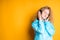 A beautiful girl listens to music with headphones putting her hands to her ears while standing on a bright background