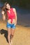 beautiful girl with long dark hair happy with the smile stands in denim shorts on the beach near the water on a Sunny day