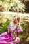 Beautiful girl with long hair braided in a braid sitting by the lake and admire the flower.