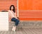 Beautiful girl with long hair brunette in jeans sits near wall of orange old white wooden planks