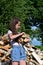 beautiful girl with long hair in white T-shirt and denim shorts puts firewood in pile.