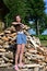 beautiful girl with long hair in white T-shirt and denim shorts puts firewood in pile. Concept of harvesting firewood for winter.