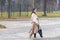 A beautiful girl with long hair with wireless headphones in her ears in a raincoat walks along the road in a deserted place