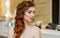 Beautiful girl, with long, red-haired hairy. Hairdresser weaves a French braid, close-up in a beauty salon