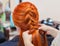 Beautiful girl with long redhair, hairdresser weaves a  braid, close-up in a beauty salon. Professional hair care and creating