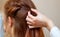 Beautiful girl with long redhair, hairdresser weaves a  braid, close-up in a beauty salon. Professional hair care and creating