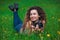 Beautiful girl-photographer with curly hair holds a camera and lying on the grass with blooming dandelions in the spring outdoors