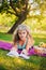 Beautiful girl on a picnic in the park is reading a book. Blonde on a purple bedspread resting. Fruit basket at a picnic