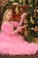Beautiful girl in pink dress decorating Christmas tree at home