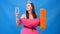 Beautiful girl in a pink dress made of pillows with a mop and a glass of wine on a blue background. Crazy quarantine