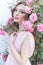 Beautiful girl in a pink dress standing in the garden roses in a sunny bright summer day with a gentle make-up and bright puf