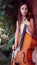 Beautiful girl in a pink dress stands with a cello in a country house with wild grapes
