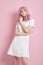 Beautiful girl with pink hair, hair coloring. Cute anime woman stands on a pink background in a short white dress. Colored hair,