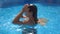 Beautiful girl pops up under water at the pool. Young woman emerges from under the water at the basin of hotel. Brunette