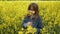 A beautiful girl with posing against a yellow rapeseed field. She smelling yellow canola flowers