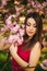 Beautiful girl posing to the photographer against the background of blooming pink trees. Spring. Sakura.