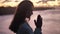 Beautiful girl praying looking up at orange sky with hope, close-up. Silhouette of young woman dreaming looking upwards