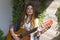 A beautiful girl with red curly hair stands and holds a seven-string guitar in her hands.