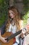 A beautiful girl with red curly hair stands and holds a seven-string guitar in her hands.